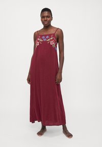 Abito maxi borgogna con spalline sottili, caratterizzato da ricami floreali in rosso e blu sullo scollo. Tessuto morbido, vestibilità ampia, lunghezza alla caviglia.