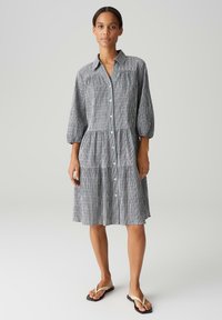 Zwart-wit gestreepte jurk met knoopsluiting aan de voorkant, kraag, driekwart mouwen en een gelaagde rok. Glad stoftextuur.