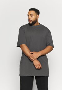 Graues, übergroßes T-Shirt mit kurzen Ärmeln, Rundhalsausschnitt und glatter Textur, kombiniert mit schwarzen Hosen. Einfaches, modernes Design.