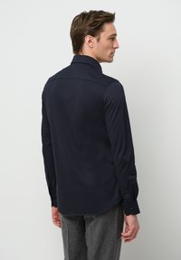 Marineblaue Langarmshirt mit spitzem Kragen, Knopfmanschetten und glatter Textur, von hinten gezeigt. Taillierte Passform und abgerundeter Saum.