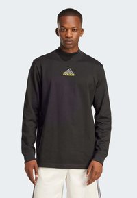 Svart langermet skjorte laget av bomull, med høy hals, Adidas-logo i gult, og en avslappet passform. Enkel design uten mønstre.