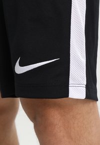 Mustat urheilushortsit, joissa on valkoinen sivupaneeli, valmistettu sileästä kankaasta, jossa on verkkotekstuuri. Lahkeessa on valkoinen Nike-logo.