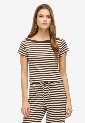 Vrouw draagt een bruin en beige horizontaal gestreept T-shirt met korte mouwen en bijpassende broek met een koord in de taille, staand tegen een witte achtergrond.