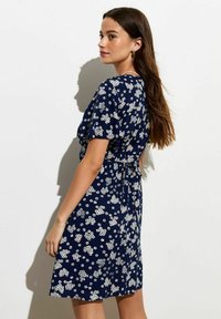 Vestido azul marino con un patrón floral blanco, mangas cortas y detalle de cintura atada; tejido ligero con un diseño fluido.