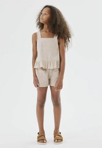 Completo in lino beige composto da due pezzi, con top senza maniche e orlo a volant e pantaloni corti abbinati, completato da sandali marroni.