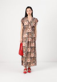 Garšīga, rakstaina kleita ar viļņainām piedurknēm zemes toņos, ar V-veida dekoltē un šķērsgriezuma dizainu. Apvienota ar sarkanu rokassomu un apaviem.