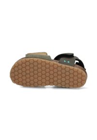 Brun sandal med en texturerad gummisula, justerbar svart rem och gröna tygdetaljer. Har ett hexagonalt greppmönster på undersidan.
