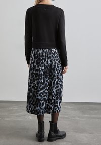 Svart kort sweatshirt med långa ärmar, tillsammans med en grå leopardmönstrad kjol. Svarta ankelboots fulländar outfiten. Slät textur.