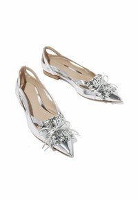 Ballerine argento con punta affilata, decorate con un fiocco e borchie, dotate di fianchi a taglio e tacco basso.