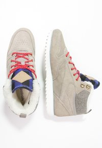 Light gray suede high-top sneakers with red laces, plush white lining, and textured gray accents; featuring a patterned blue tongue and white sole.