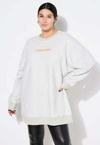 Felpa oversize grigia chiara con il testo arancione "COOL & KIND". Presenta polsini e orlo a coste, e un tessuto morbido e testurizzato.