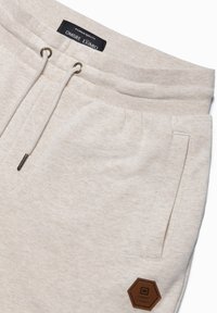 Lichtbeige sweatpants van zacht materiaal, met een drawstring met metalen uiteinden, zijzakken en een hexagonale logo patch.