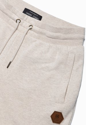 Pantalons de jogging beige clair en tissu doux, dotés d'un cordon de serrage avec des embouts en métal, de poches latérales et d'un patch logo hexagonal.