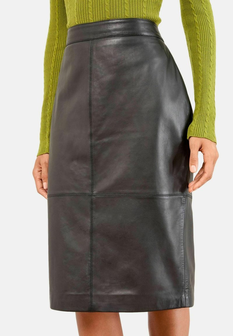 Juodas odinis pieštuko sijonas su aukštu liemeniu, su panelių siuvinėjimais ir lygiu paviršiumi, derinamas su žaliu struktūruotu megztiniu.