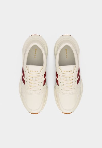 Paire de baskets blanches en cuir avec des bandes latérales bordeaux, des lacets et le logo "BALLY" doré sur la languette et la semelle intérieure, vues de dessus.