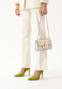 Τσάντα ώμου από ανοιχτό γκρι δέρμα με χρυσές λεπτομέρειες, ορθογώνιο σχήμα και αλυσίδα-χέρι, συνδυασμένη με λευκά κομμένα παντελόνια και πράσινα τακούνια.