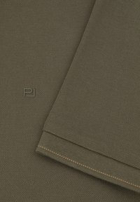 Olive zielony teksturowany materiał o wzorze tkanym. Posiada małe logo oraz kontrastowy pomarańczowy szew wzdłuż krawędzi. Gładki i solidny.