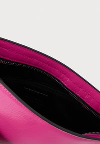 Rozā ādas soma interjers ar melnas krāsas auduma oderējumu un daļēji atvērtu melnas zipa nodalījumu.