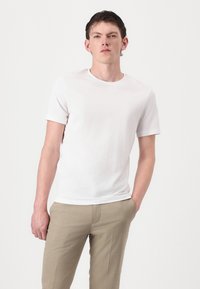 White short-sleeve cotton t-shirt with a round neckline, paired with light beige trousers. Smooth texture, fitted design.