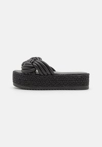 Sandale à plateforme noire avec semelle en corde tressée et straps noués rembourrés, présentée sur fond blanc uni.