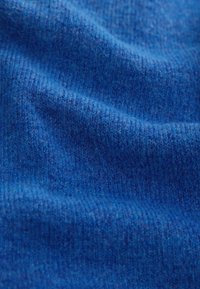 Detailní záběr měkké modré pleteniny ukazující jemnou texturu stehů a jemné záhyby.