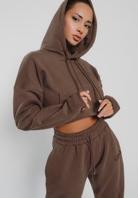 Brauner, gekürzter Hoodie mit einer Fronttasche, Kordelzug und gerippten Bündchen, kombiniert mit passenden Jogginghosen mit elastischem Bund und Stickerei.