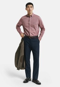 Rotes und weißes kariertes Hemd mit Knöpfen, dunkelblaue Hose, braune Lederschuhe und ein braunes, strukturiertes Sakko mit Ellbogenpatches.