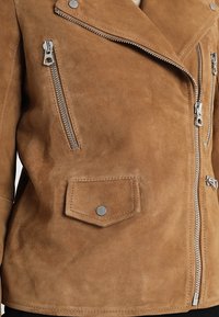 Hnědá zateplená koženka s krátkým střihem, stříbrnými zipy, kapsou na druk a klopovým límcem. Měkká textura a přiléhavý střih.