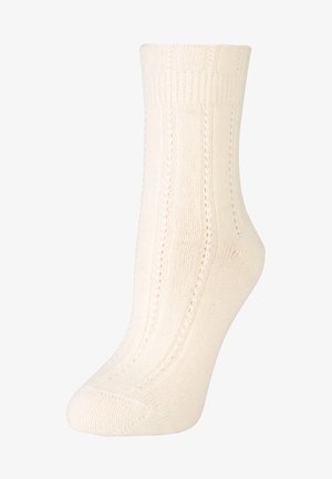 Cremefarbene Stricksocke mit geripptem Bündchen, vertikalen Mustern und glatter Textur, die für Komfort und Passform entworfen wurde.