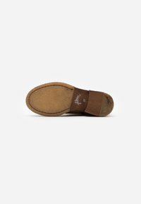 Calzature marroni con tomaia in suede e suola in sughero testurizzata. Punta arrotondata con dettagli di cucitura e branding discreto sulla suola.