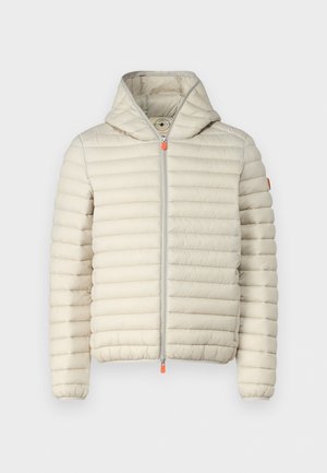 Veste matelassée beige avec capuche, fermeture éclair à l'avant et accents orange. Associée à un pantalon en denim à jambes larges et des baskets noires. Design soigné et minimal.