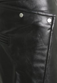 Jupe en cuir noir avec une finition texturée, des accents en métal et une coupe diagonale avec des détails de couture minimaux.