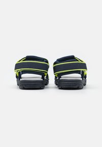 Mörkblå sandaler med gula accenter, som har justerbara remmar och en texturerad svart sula. Öppen design med vadderade områden för komfort.