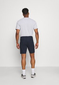 Grijs T-shirt met korte mouwen, gecombineerd met een marineblauwe short. De short heeft een soepele textuur en twee achterzakken. Gedragen met witte sokken en sneakers.