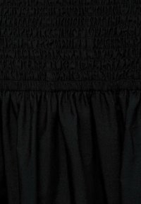 Detail černé látky se nabíraným elastickým lemem v horní části, přecházející do volně splývajícího materiálu níže.