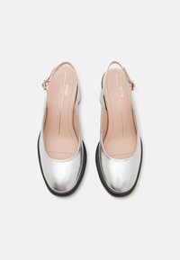 Metalické strieborné slingback topánky s hladkým povrchom, okrúhlou špicou a čiernou podrážkou. Obsahujú úzky popruh na členku so striebornou sponou.