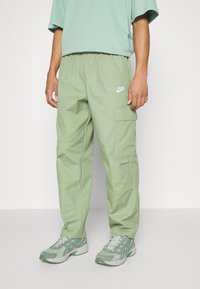 Ljusgröna cargobyxor med elastisk midja, sidfickor och en vit Nike-logotyp framtill. Matchas med matchande sneakers.