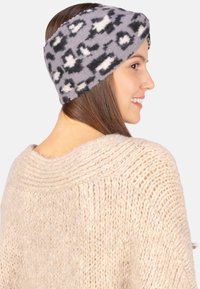 Bandeau en polaire gris et noir à motif, avec un design torsadé, porté sur la tête d'une personne, sur fond neutre.