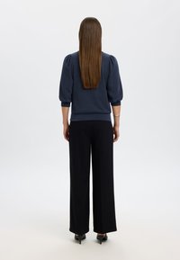 Granatowy sweter z bufkami, zestawiony z czarnymi spodniami o szerokich nogawkach i czarnymi szpilkami; gładka tkanina o luźnym kroju i ściągaczach przy rękawach.