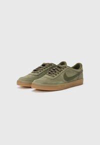 Oliwkowe sneakersy o zamszowej fakturze, z okrągłym noskiem, sznurowanym zapięciem i gumową podeszwą. Zawierają detal z logo z boku.