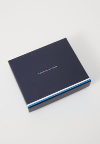 Granatowa prostokątna pudełko z białymi i czerwonymi paskami; logo "TOMMY HILFIGER" nadrukowane na środku w białym kolorze. Gładka powierzchnia.