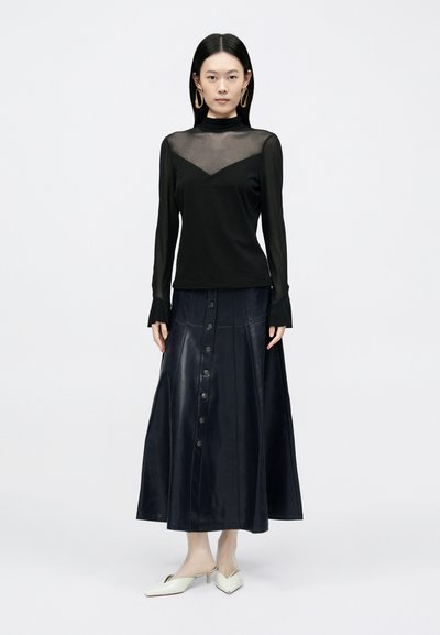 Fekete, hosszú ujjú felső hálós nyakkivágással, sötétkék, gombos bőr szoknyával párosítva. Fehér, hegyes orrú, magassarkú papucs teszi teljessé az összhatást.