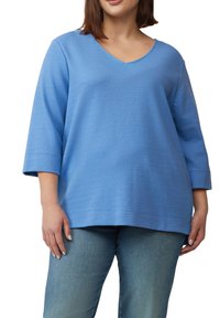 Blauwe textuur trui met een V-hals, ¾ mouwen en een losse pasvorm. Gecombineerd met lichtblauwe jeans die een eenvoudig, casual ontwerp laten zien.