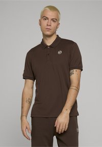 Brązowa koszulka polo wykonana z gładkiej tkaniny, z kołnierzykiem, trzema guzikami, bocznymi paskami oraz haftowanym logo na piersi.