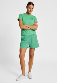 Grøn bomulds T-shirt med rund hals og korte ærmer, parret med matchende shorts. Har et blåt logo på begge beklædningsgenstande. Sneakers inkluderet.