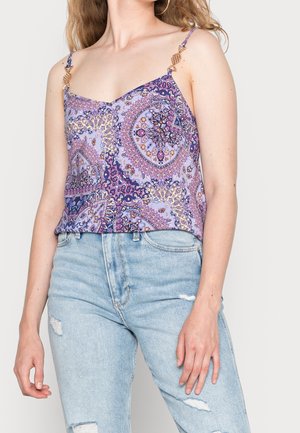Lila gemustertes Camisole mit verstellbaren Trägern und dekorativem goldfarbenem Metall. Kombiniert mit hellblauen, zerstörten Jeans.