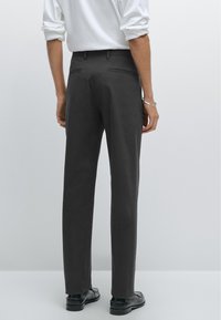 Pantaloni grigi scuri su misura con una finitura in tessuto liscia, due tasche posteriori e un design a gamba dritta, abbinati a scarpe nere.