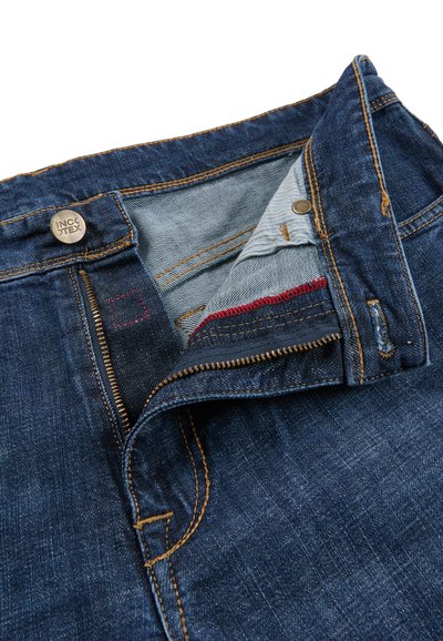 Dark blue denim jeans with open zipper and button fly showing inner fabric lining and contrast red stitching.