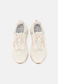 Chaussures de sport légères en beige et rose pastel. Elles disposent d'une tige en maille respirante, d'une semelle amortissante et d'un système de laçage. Accent dénotant une marque.