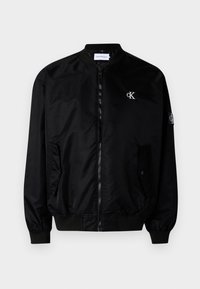 Čierna bomber bunda vyrobená z hladkého nylónu. Obsahuje predný zips, rebrové manžety a golier, s malým logom na hrudi a rukáve.